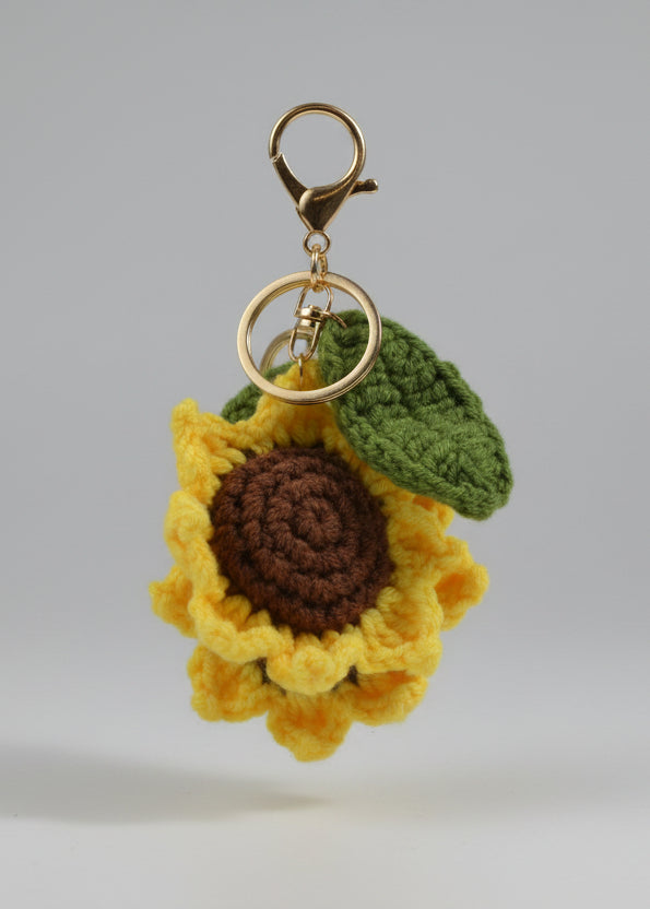 Crocheted sunflower keychain with a green leaf on a metallic surface.