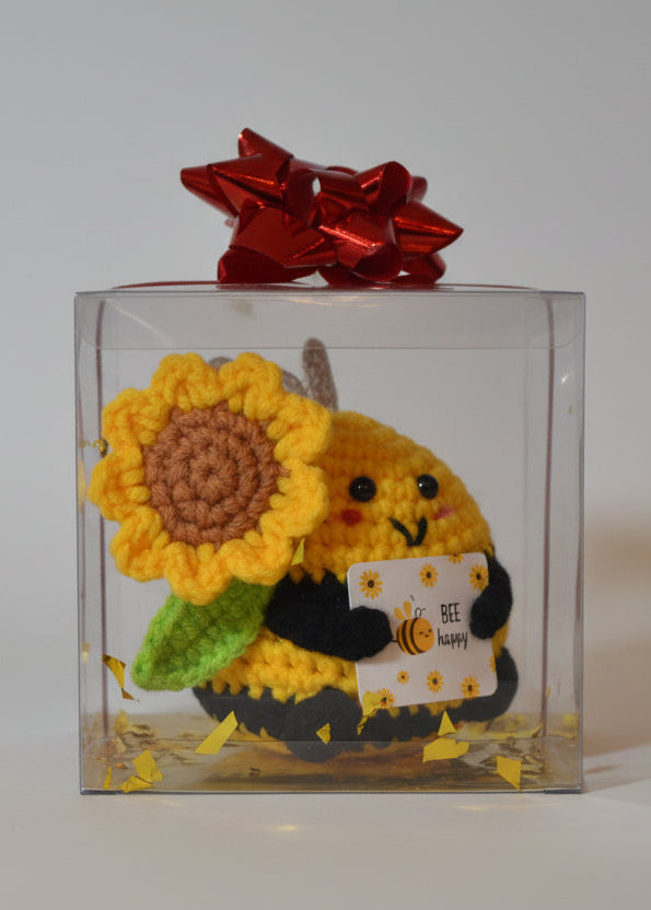 Crocheted bee with a sunflower on a clear stand with a red bow in the background.