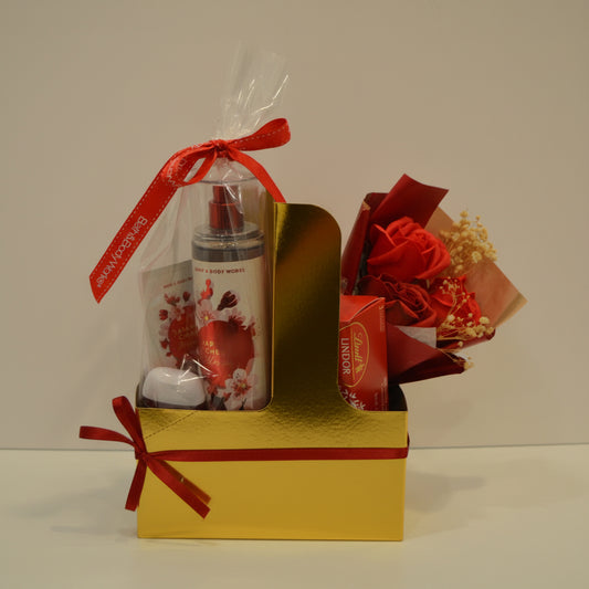 Gift set with a bottle, small bag, and bouquet in a brown box with a red ribbon on a white background.